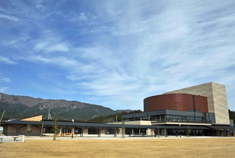 青い空と後方の山々と共に市民文化会館全体の外観を撮影した写真
