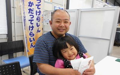 窓口の椅子に座り子供を膝にのせて笑顔を見せる男性の写真