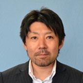 青い背景にジャケットを着て笑顔を向ける山中光茂氏の写真