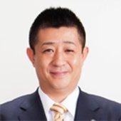 黄色いネクタイとスーツを身にまとった井原巧氏の写真