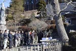 華蔵寺に生えている宝珠マツの伐採にあたり宝珠マツの前に祭壇を構えお経を唱える住職とその後ろで両手を前に組み神妙な面持ちで並んでいる関係者らの写真