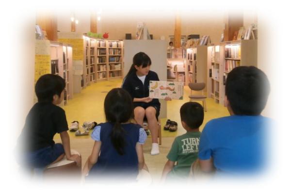 児童たちの前で絵本を読み聞かせているボランティアの写真