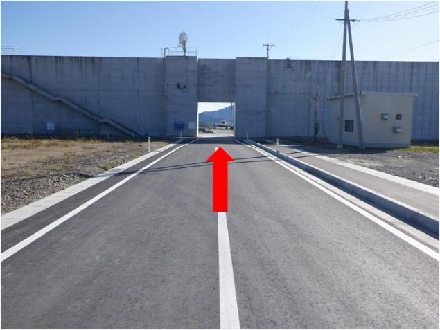 道路部分が開いているコンクリートの壁に向かい、直進する赤い矢印が付いている写真