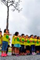 黄色いお揃いのシャツを着た児童たちが一本松の前に並んで立っている写真