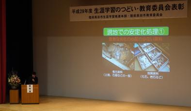 陸前高田市コミュニティホールの一室でプロジェクターを使用しながら壇上で被災紙製資料の安定化処理について説明する市教育委員会の浅川氏の写真