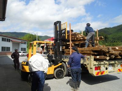 木材運搬機に置かれた残存部材の上に乗りさらに部材を乗せる男性2人とその様子を運搬車の前から見守る男性3人と運転者の男性の写真