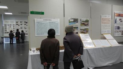 陸前高田市コミュニティホールの一室に展示された数々の文化財の壁に貼られた説明パネルを熟読する2人の来場者の女性を背中側から撮影した写真