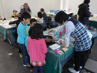 陸前高田市コミュニティホールの一室でおこなわれた体験コーナーで女性職員の説明を熱心に聞く子供たちの写真