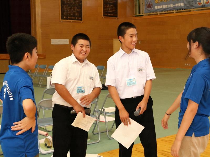 陸前高田市立第一中学校の体育館で男子生徒2人と楽しそうに会話をする左端の青色のポロシャツを着た名古屋市の女子中学生と右端の男子中学生の写真