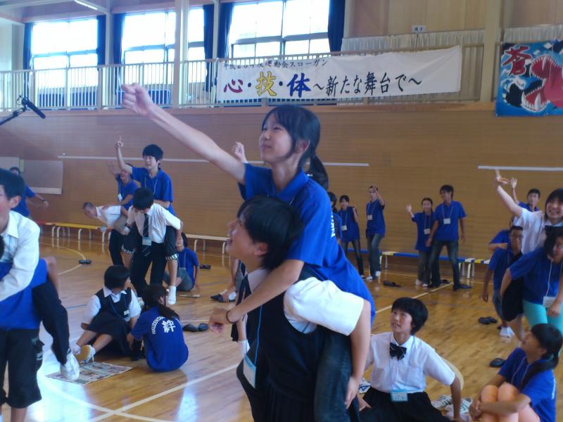陸前高田市立第一中学校の体育館で陸前高田市の中学生たちと名古屋市の中学生たちがお互いにおんぶをし背負われている方は前方に向かって右手を突き出しじゃんけんをしている写真
