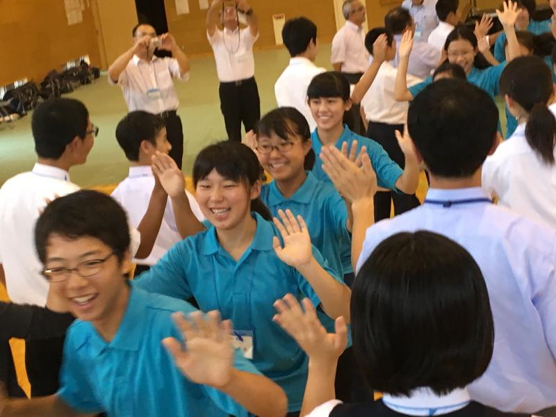 陸前高田市立第一中学校の体育館で両端に並ぶ生徒らの間をはにかみながらハイタッチして歩く水色のポロシャツを着た名古屋市の中学生たちの写真