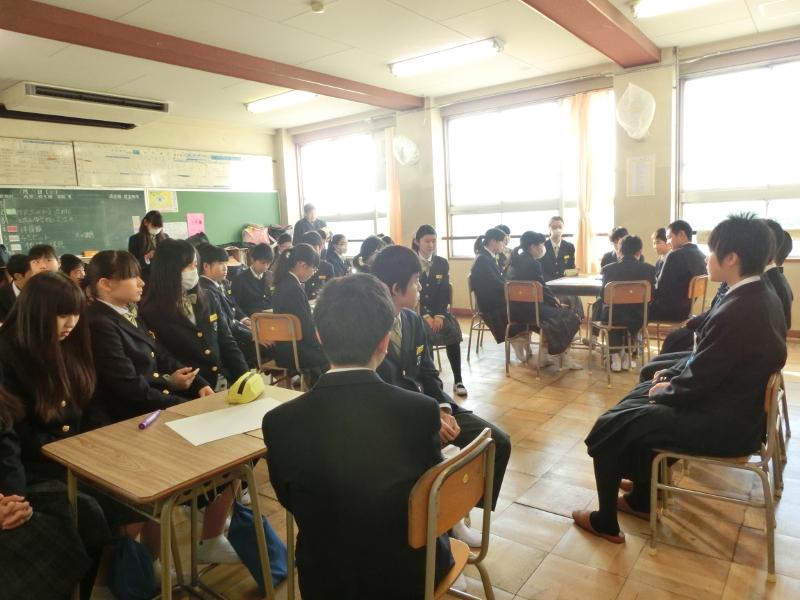 名古屋市立城山中学校の教室で横並びに椅子に座る陸前高田市の中学生たちの前方で両手に持った紙を読みながら歓迎の挨拶をする女子生徒の写真
