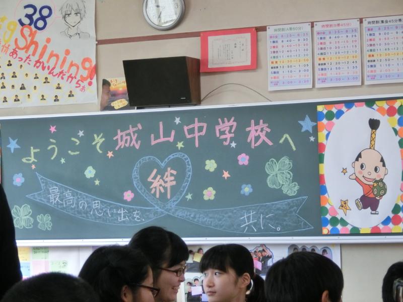 名古屋市立城山中学校の教室の黒板にカラフルなチョークでようこそ城山中学校へと書かれた下にハートマークのリボンが描かれハートの中には絆の文字がリボンには最高の思い出を共にと書かれた写真