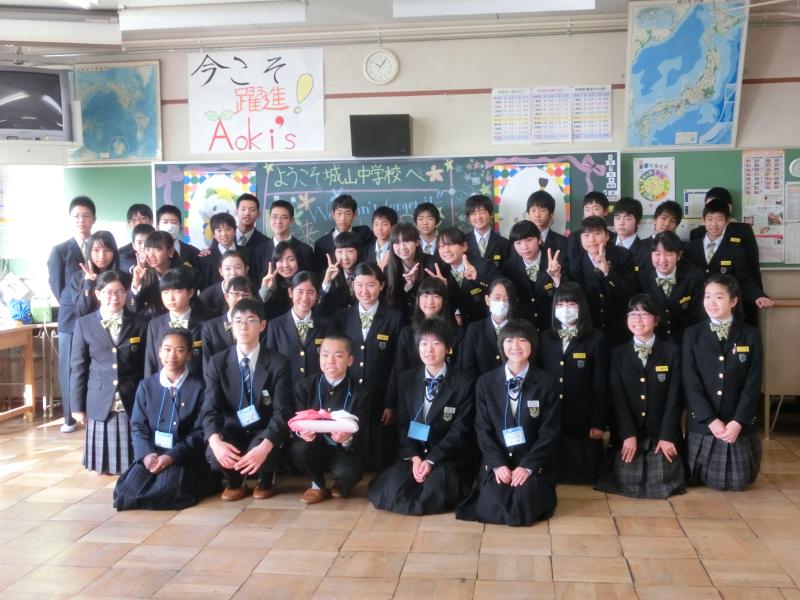 名古屋市立城山中学校の教室で黄色のチョークでようこそ城山中学校へ書かれた黒板の前で記念撮影をする陸前高田市の中学生たちと生徒たちの写真