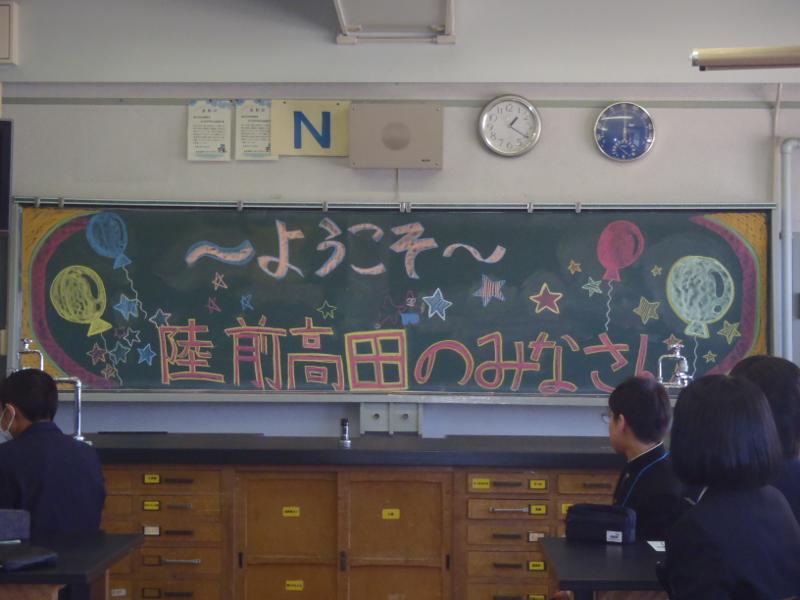 中学校の教室の星や風船に囲まれてようこそ陸前高田のみなさんと書かれた黒板を座りながら眺める中学生たちの写真