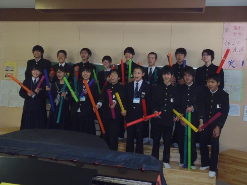名古屋市内の中学校の教室にあるグランドピアノの前で縦2列で8人ずつ横に並びカラフルな棒を持ち楽しそうな表情を浮かべる中学生たちの写真