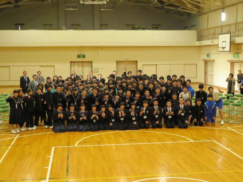 名古屋市内の中学校の体育館で1列目の中学生たちは正座をして2列目の中学生たちは中腰になりその他の生徒らは起立で記念撮影をする写真