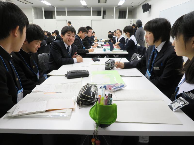 数人一グループになって白色の会議用の横長机にノートやペンケースを置いて交流を深める中学生たちの写真