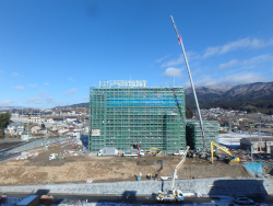 青空の下、背の高い重機の横に、重機の半分くらいの高さの庁舎が建っている2020年12月の進捗状況の写真